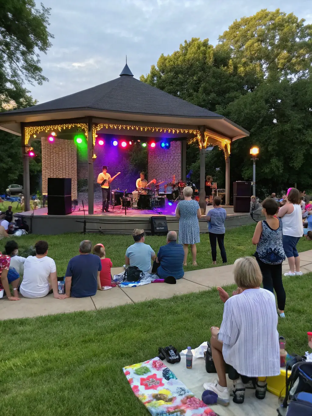 A wide shot of a well-attended COMITE DES FETES event, showing a diverse crowd of people enjoying live music and local food, highlighting the event's popularity and inclusivity.